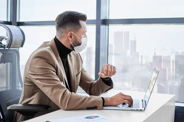 Fototapeta premium businessman in a protective mask working on a laptop in the office.