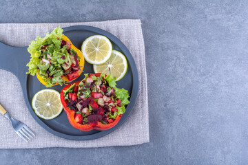 Lemon slices with two portions of salads in pepper slices on a serving pan on marble background