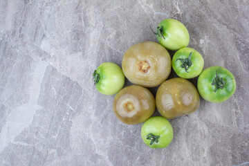 Fresh green tomatoes and pickled tomatoes on marble surface