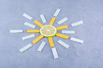 Neatly arranged chewing gums centering on a slice of lemon on marble background
