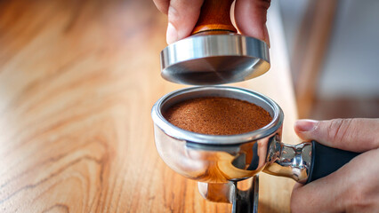 Close-up of hand Barista cafe making coffee with manual presses ground coffee using tamper on the wooden counter bar at the coffee shop