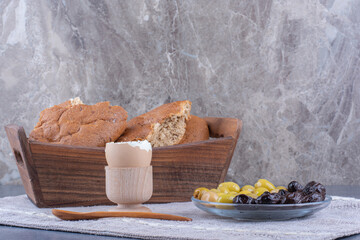 Modest breakfast set with bread, egg and olives on marble background