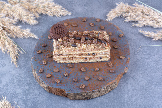 Cake topped with coffee beans and biscuit on a board next to needlegrass stalks on marble background