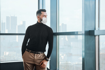 businessman in a protective mask standing near the window.