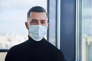 young man in a protective mask standing near the window.