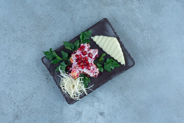 Sliced and grated cheese on a black platter with a small portion of salad, on marble background