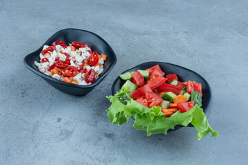 Shepherd's salad next to pepper and cauliflower salad on marble background