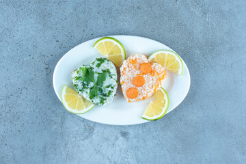 Cooked rice with greens and carrots, garnished with lemon slices on marble background