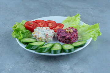 Salad assortment decorated with cucumber and tomato and lettuce leaves on marble background