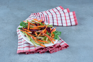 Carrots, cucumbers and beetroots chopped into a snack salad on a platter on marble background