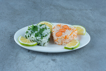 Platter of cooked rice with greens and carrots, garnished with lemon slices on marble background