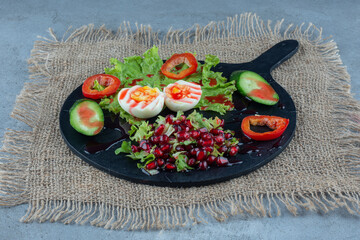 Serving tray reakfast made of boiled eggs, cucumber and pepper slices and pomegranate salad on marble background