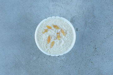 Bowl of oatmeal topped with handful of raisins on marble background