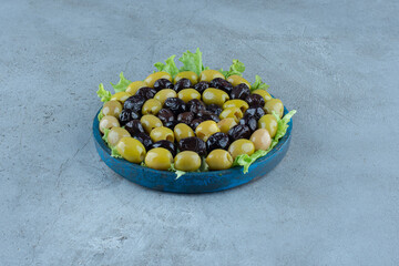 Assortment of olives on a lettuce covered platter on marble background