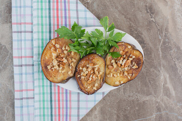 Delectably flavored platter of fried indian eggplant slices garnished with chopped garlic and parsley, on marble background