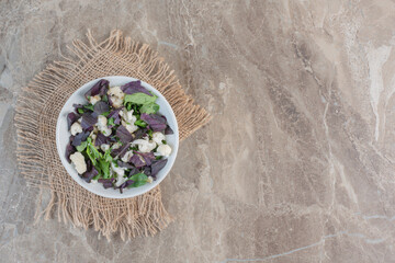 Small plate of appetizing light salad mix of amaranth, basil leaves and cauliflower on marble...