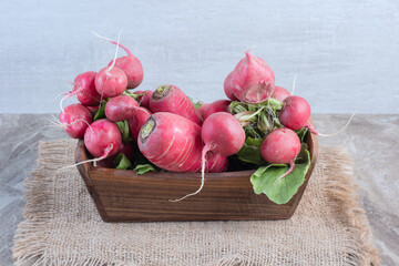 Wooden bowl of bundled up turnips on a piece of cloth on marble background
