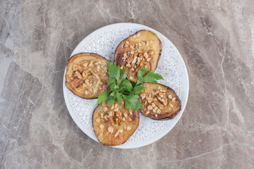 Indian eggplant fried and seasoned with garlic on a platter, adorned with parsley on marble background