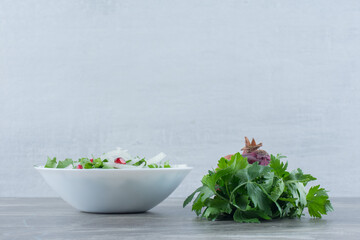 Cilantro, onion and pomegranate made into a salad in a bowl on marble background