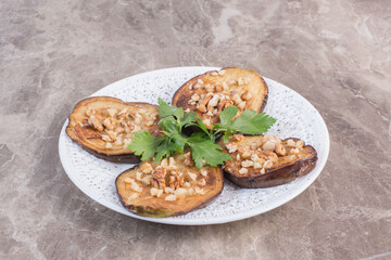 Sliced indian eggplant fried and seasoned with garlic on a platter, adorned with parsley on marble background