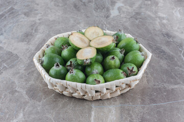 Feijoa piled in a white basket and adorned with feijoa slices on marble background