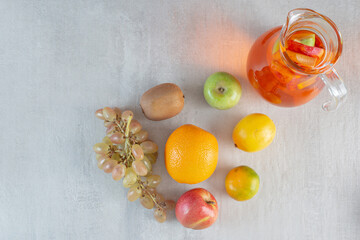 A glass jug of juice with fruits on marble background