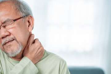 Asian Senior elderly man feek neckache his touching neck pain. Streesed old male suffer while sit on sofa at home. Health care and insurance retirement concept.