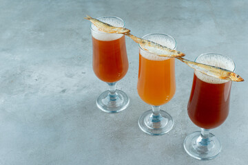 Three glasses of light beer with fish on gray background