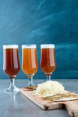 Three glasses of beer with fish and cheese on wooden cutting board