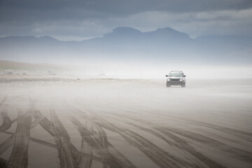 tire marks left in the sand from trucks driving on the beach with a SUV comming out of the fog