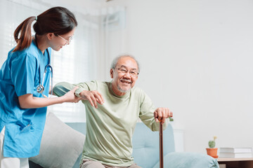 Obraz premium Asian senior elderly man patient doing physical therapy with caregiver. woman nurse helping get up from wheelchair for practice walking with walker at home, practice walk slowly at nursing home care.