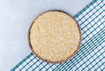 Cleaned and dried brown rice stocked on a large wooden tray on a laid-out tablecloth on marble background