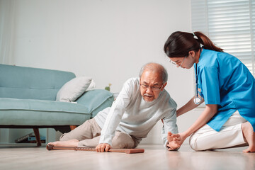 Obraz premium Asian caregiver helping senior male from falling on the ground. Older elderly man patient having accident heart attack when physical therapy. Nurse assistance rescue concept.