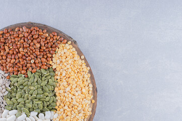 Slice of log topped with red beans, pepitas, navy beans, red lentil and peeled sunflower seeds on marble background