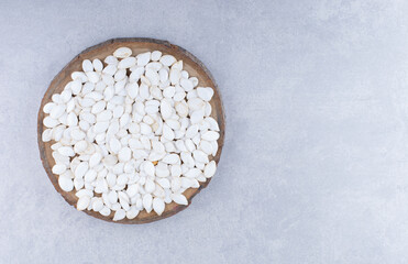 White pumpkin seeds laid out to dry on a sliced pieced of log on marble background