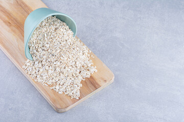 Blue bowl pouring oat on a wooden tray on marble background