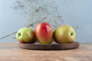 Three fresh apples with withered flower on wooden board