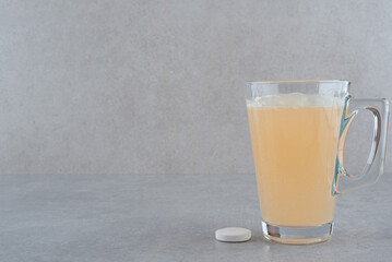 A glass of cure and tablet on gray background
