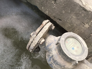 A water flow meter that delivers industrial wastewater to a wastewater treatment plant. Water is yellowish and foamy