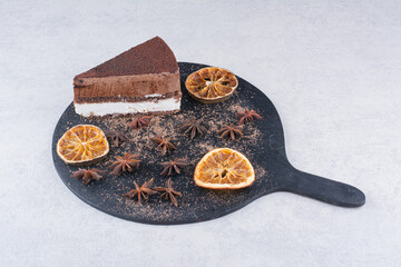 Slice of chocolate cake with cloves and orange slices on dark board