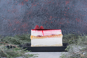 Slice of cheesecake on black board with pine branch
