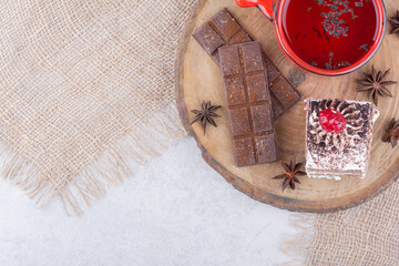 Cup of tea, cake slice and chocolate bar on wooden piece