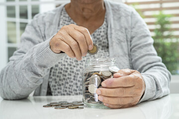 Asian senior or elderly old lady woman holding counting coin money in glass jar. Poverty, saving...