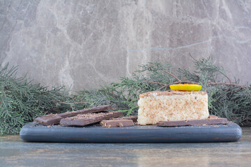 A piece of tasty cake with sliced chocolate on dark board