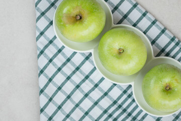 Whole green apples on white plates with striped tablecloth
