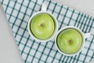 Whole green apples in white cups with tablecloth