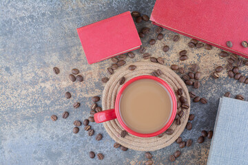 A cup of coffee with book and coffee beans on marble background