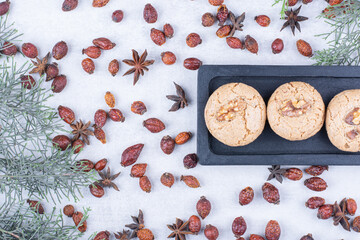 Delicious walnut cookies on dark plate with rosehips
