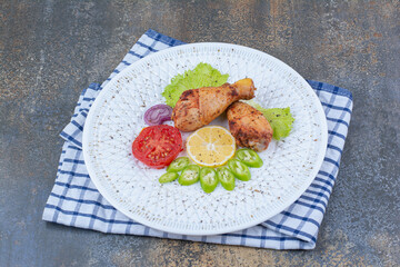 Grilled chicken drumsticks on white plate with vegetables