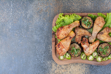 Roasted chicken legs and wings on wooden board with lettuce and pepper
